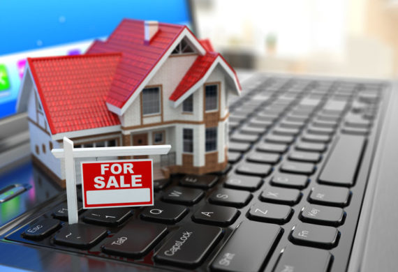 A Small toy model of a home and a for sale sign displayed on the keyboard of a laptop